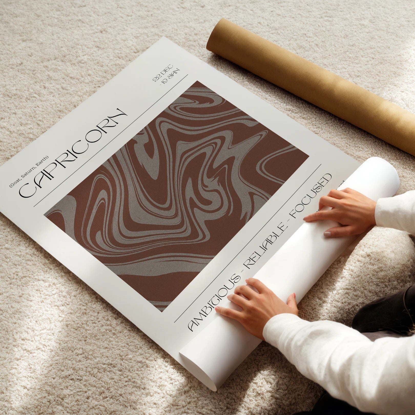 Person unrolling a poster roll with Capricorn zodiac design on a light surface