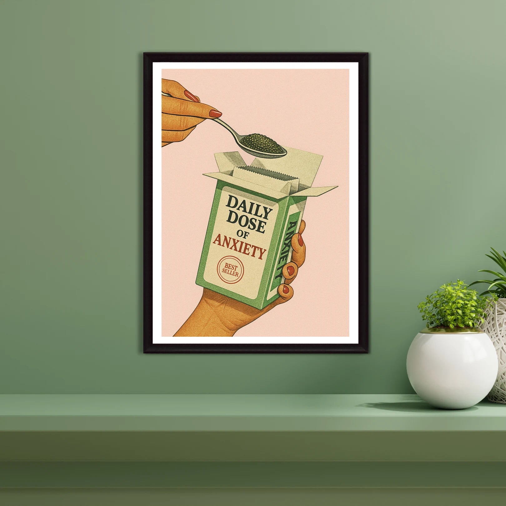 Framed artwork of a hand holding a box labeled 'Daily Dose of Anxiety' on a green wall.