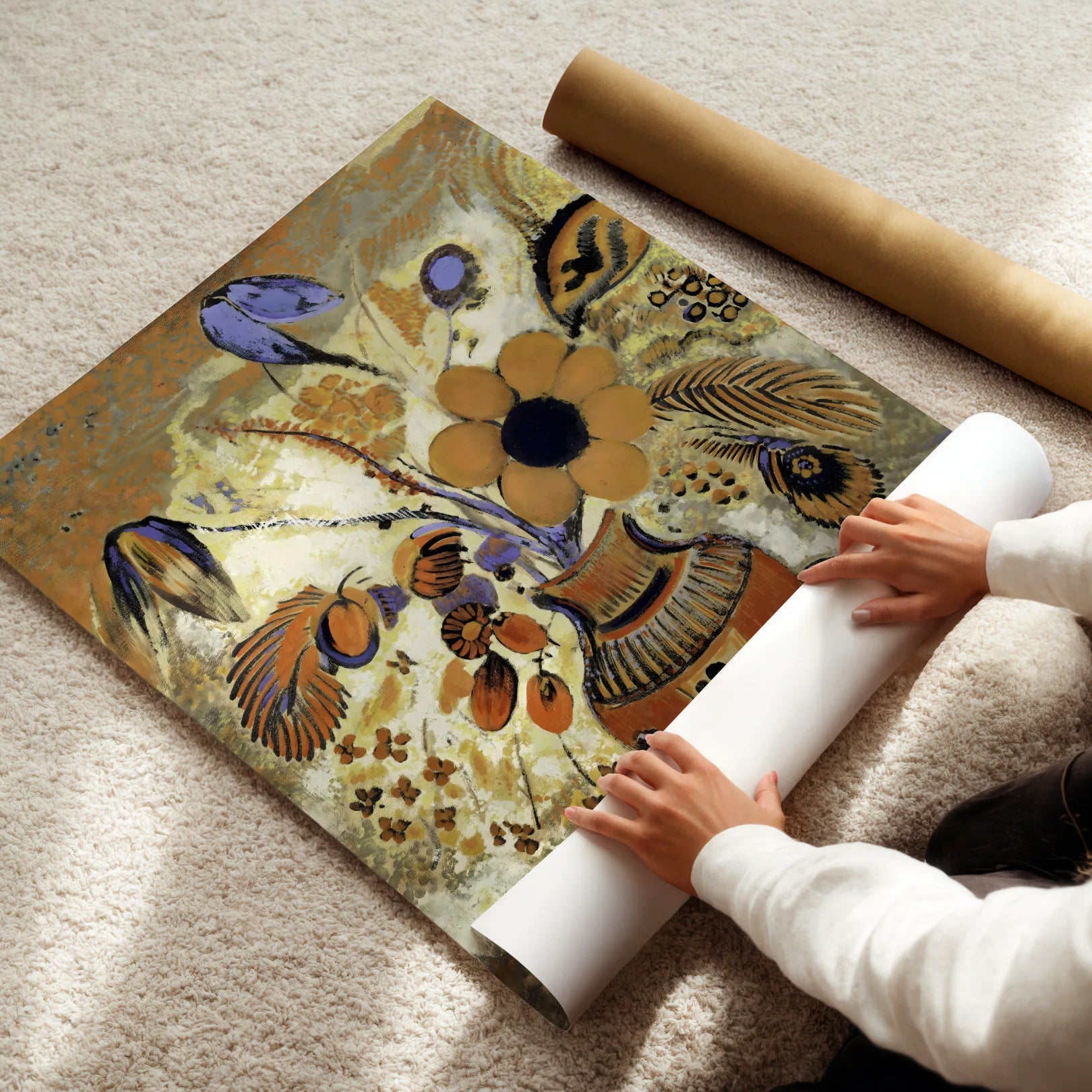 Person unrolling a decorative poster with floral and peacock feather design on a light-colored floor.