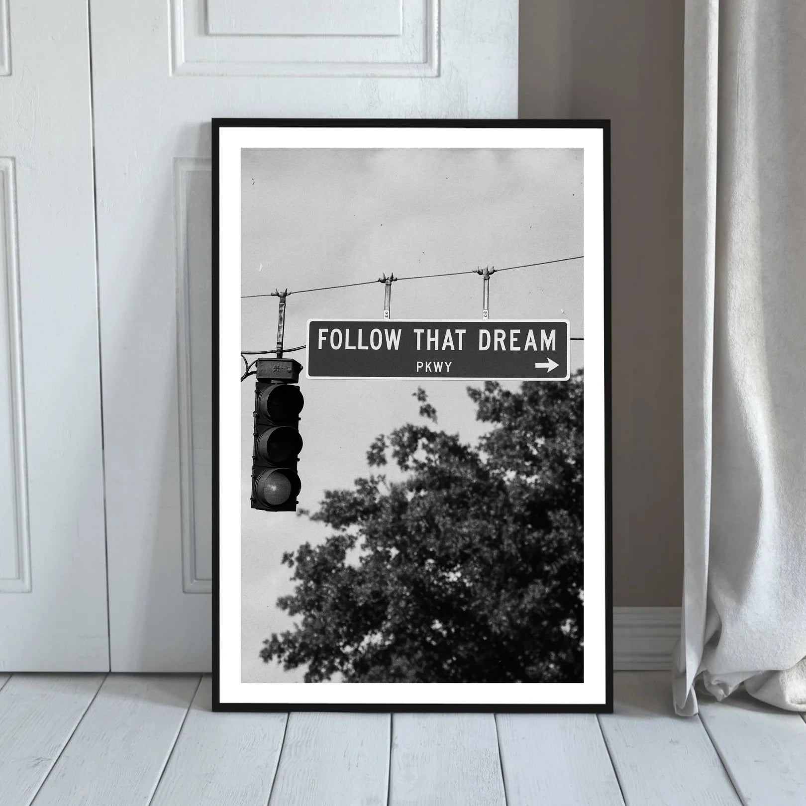 Framed poster with 'Follow That Dream' sign and traffic light against a white wall.