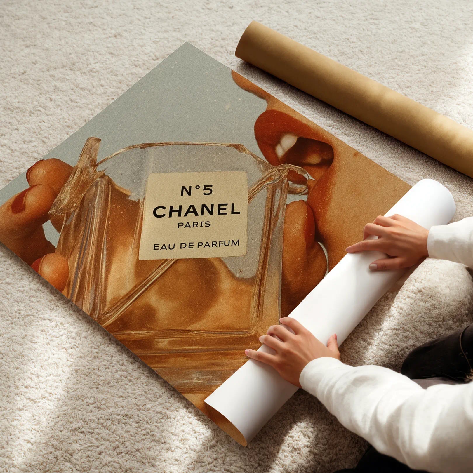 Person unrolling a Chanel No. 5 perfume bottle art poster on a textured surface.