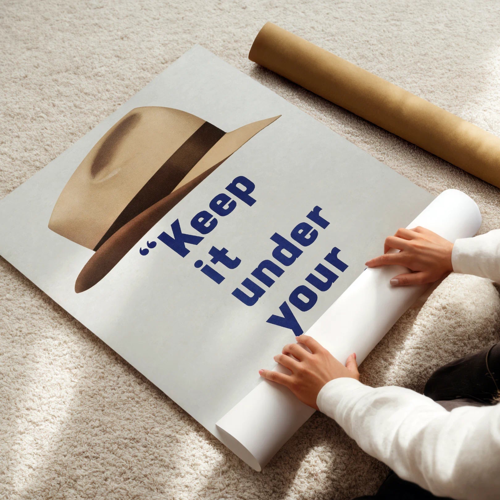 Person unrolling a poster with text 'Keep it under your' on a carpeted floor.