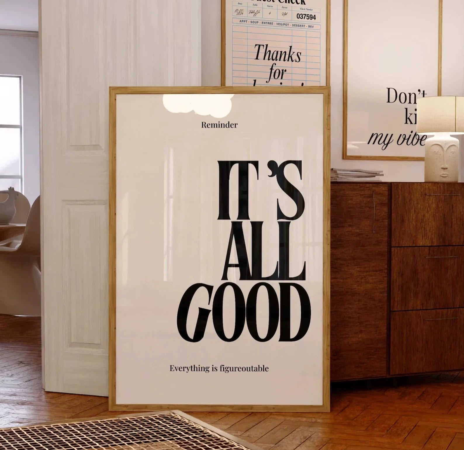 Framed poster with 'It's All Good' text in a room with wooden furniture and framed pictures on the wall.