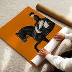 Person unrolling a large Hermes poster of a horse and rider on an orange background.