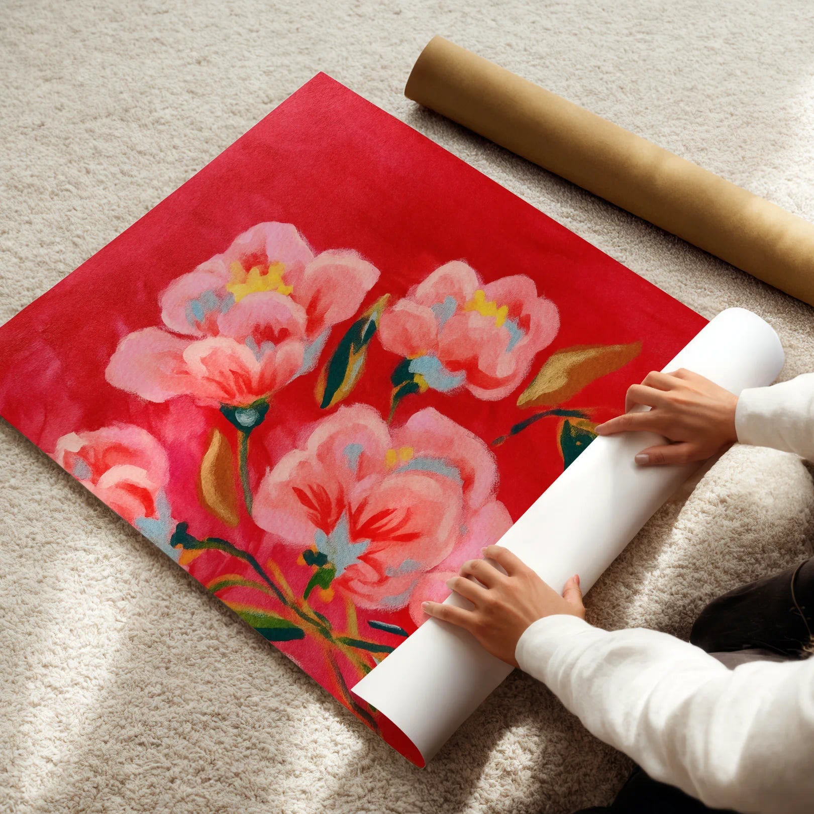 Person unrolling a floral poster with pink flowers on a beige carpet