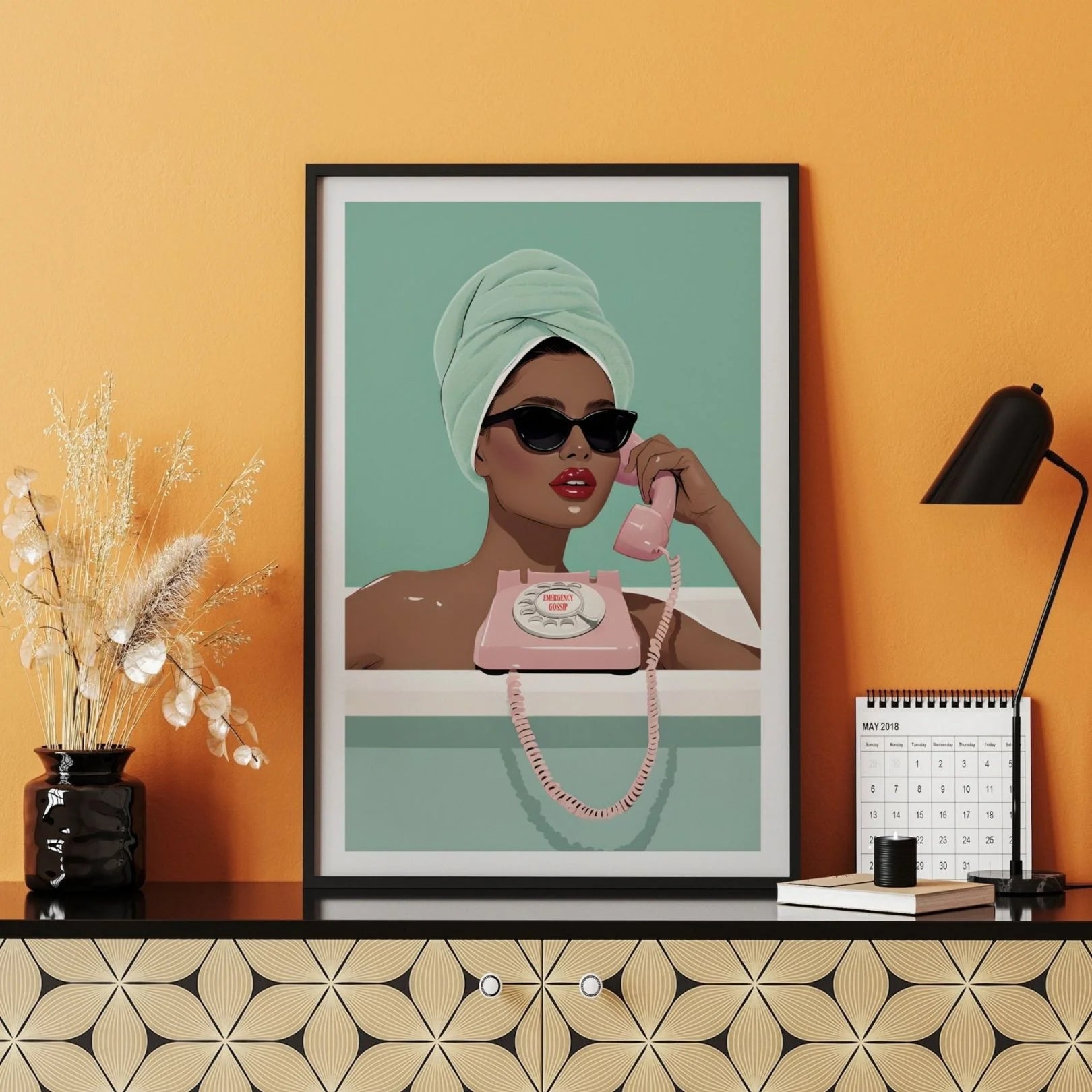 Emergency Gossip retro-style art print leaning on patterned cabinet with orange wall and dried flowers