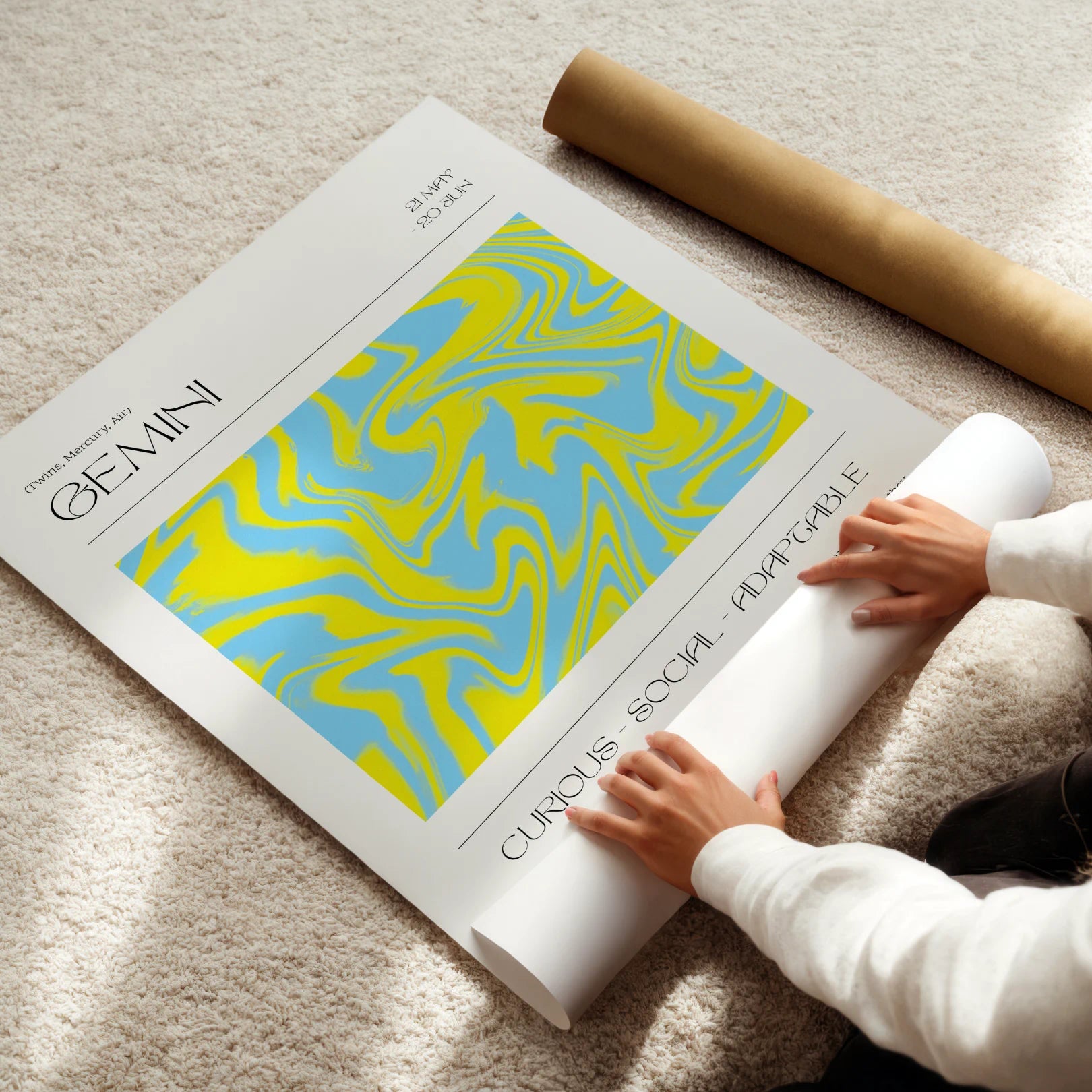 Person unrolling a large gemini poster with abstract design and text on a carpeted floor.