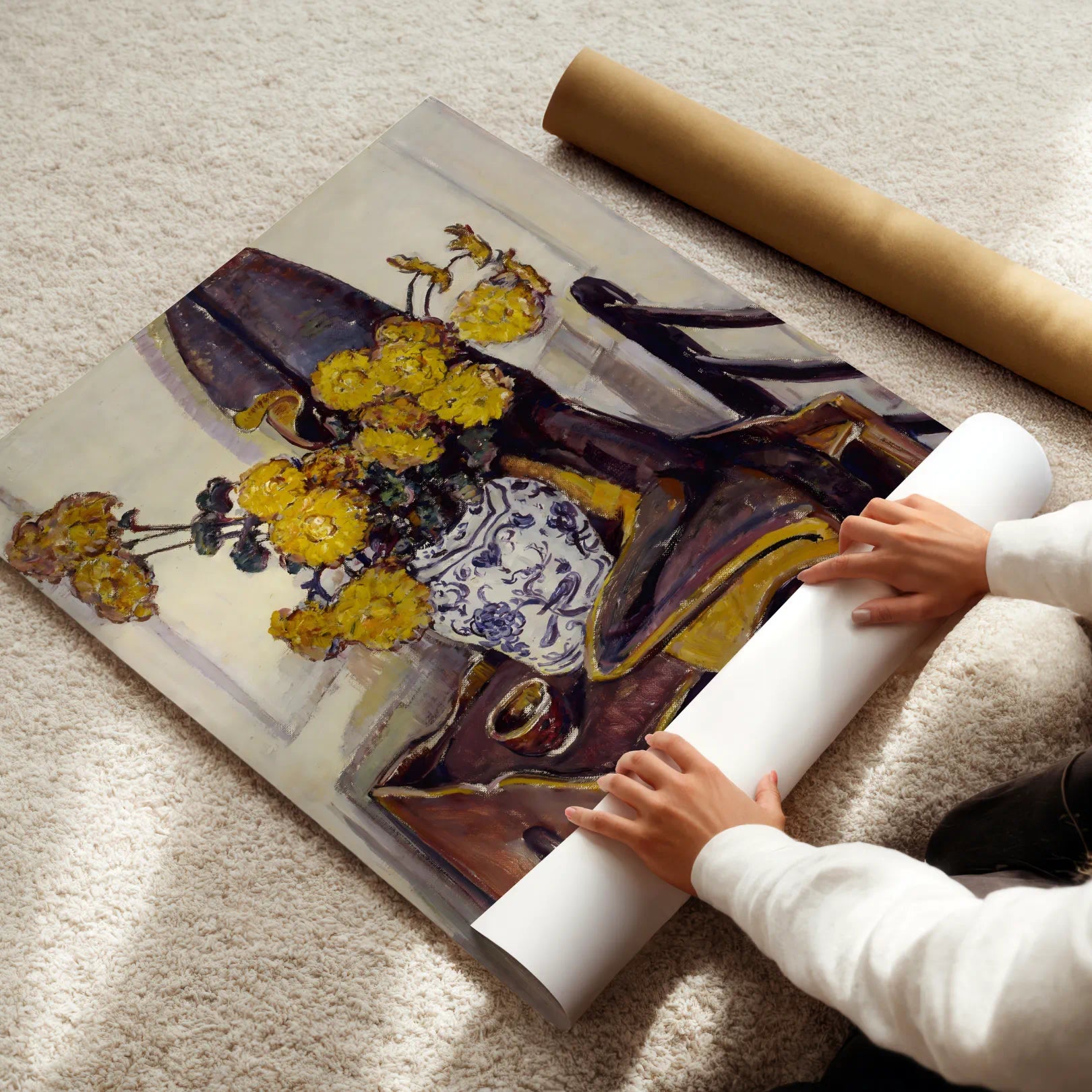 Person unrolling a large poster of a still life with yellow flowers and a purple vase on a light-colored floor.