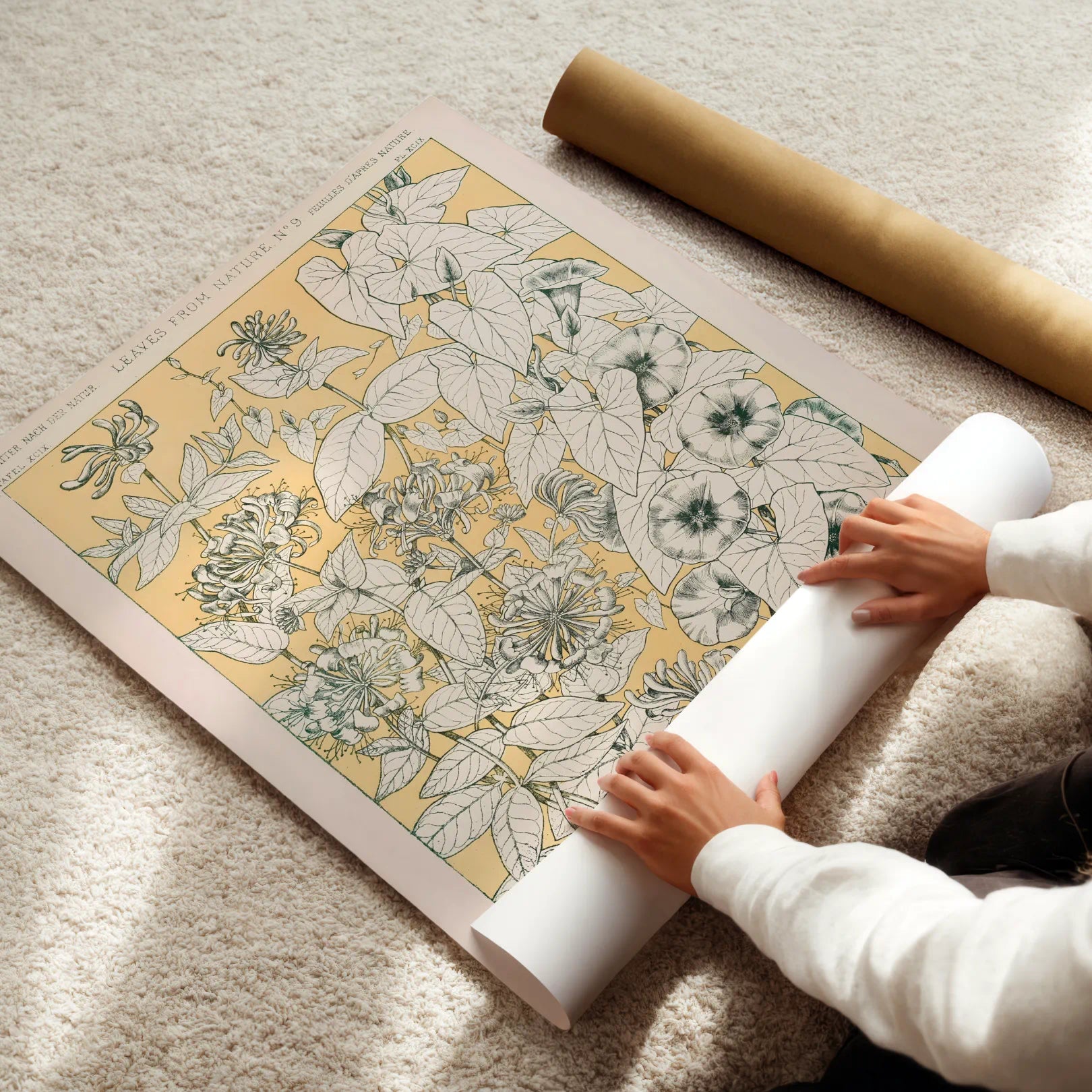 Person unrolling a floral-patterned paper on a light-colored floor.