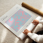 Person unrolling a large poster with a pink and blue libra zodiac design on a light-colored floor.