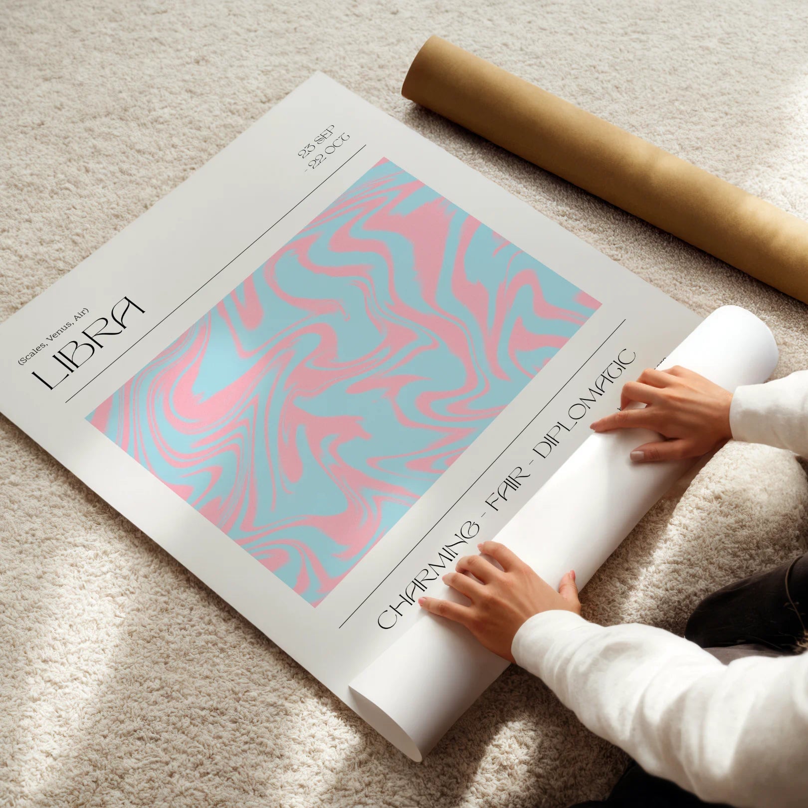Person unrolling a large poster with a pink and blue libra zodiac design on a light-colored floor.