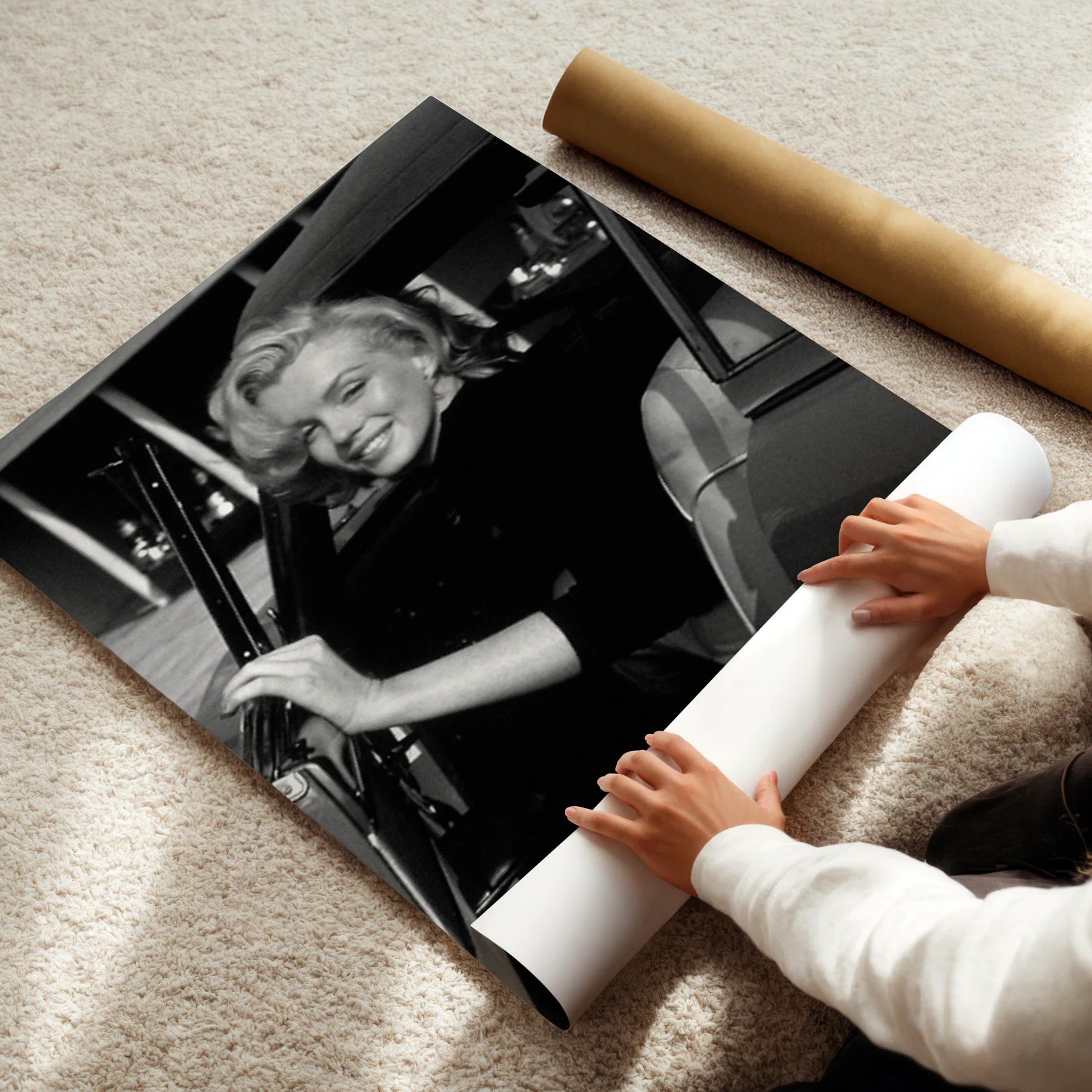 Person unrolling a large black and white photograph of Marilyn Monroe on a carpeted floor.