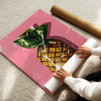 Person unrolling a pink poster with a pineapple design on a carpeted floor.