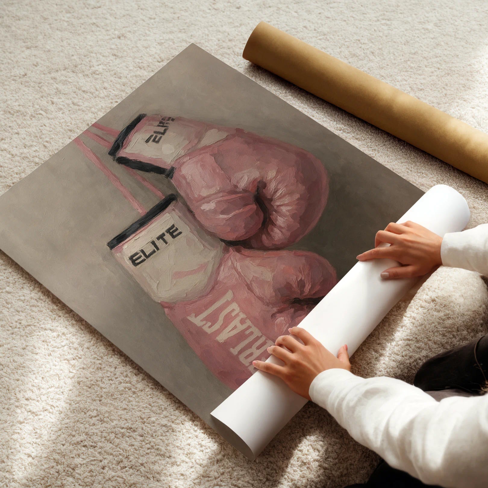 Person unrolling a poster of pink boxing gloves on a light-colored floor.