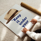 Person unrolling a poster with text 'Keep it under your' on a carpeted floor.