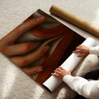 Person unrolling a large poster of a intimate book poster art on a light-colored floor.