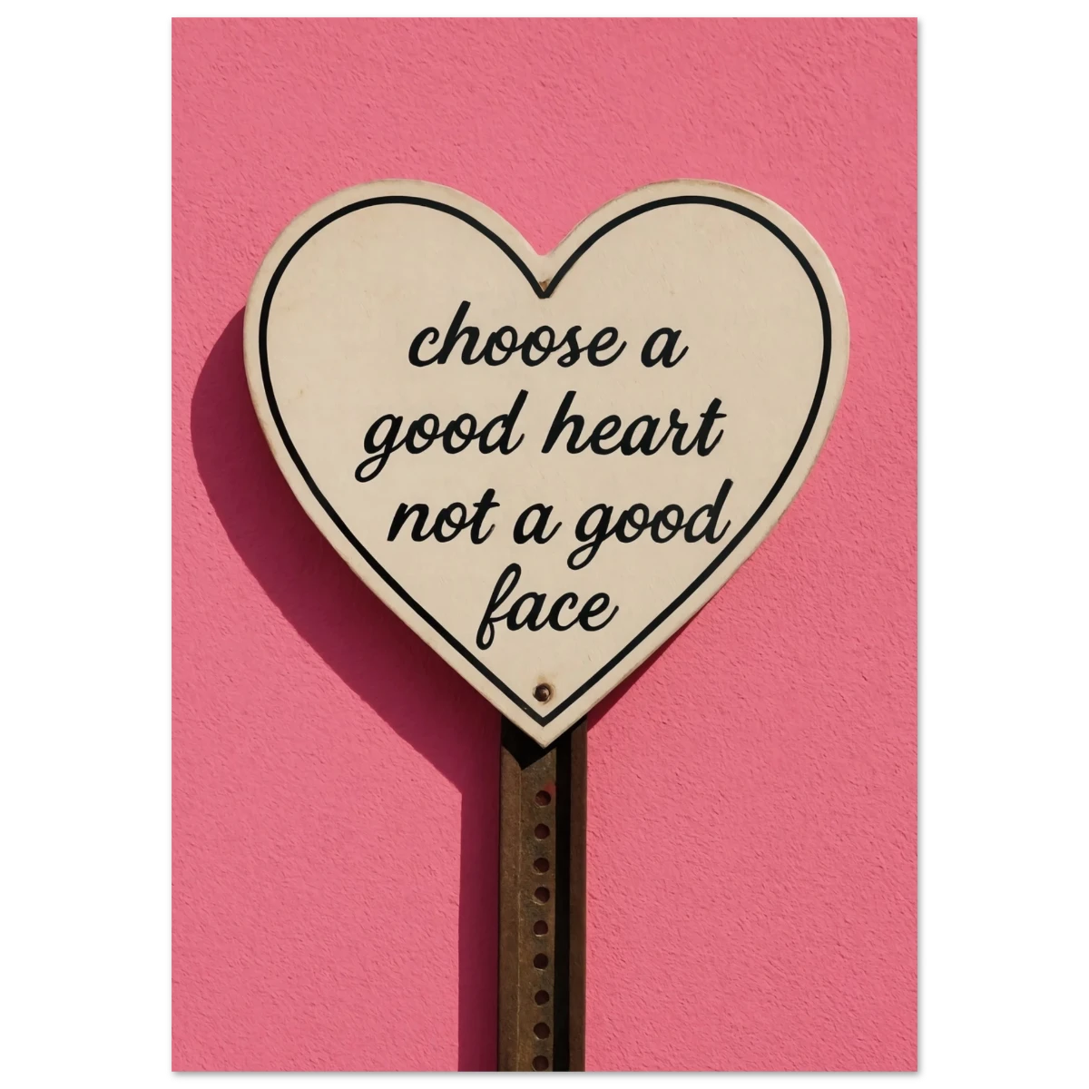 Heart-shaped sign with 'choose a good heart not a good face' text on a pink background