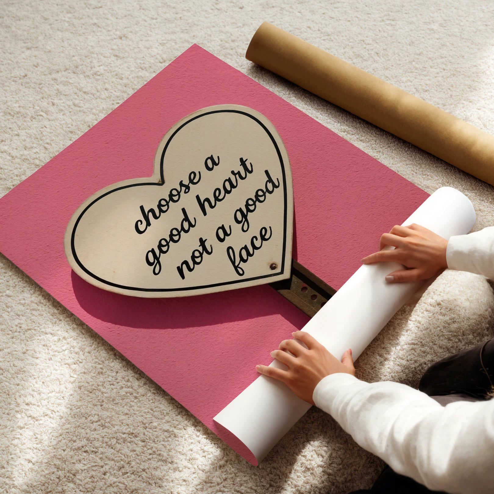 Person unrolling a pink mat with a heart-shaped sign on a beige carpet.