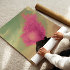 Person unrolling a large pink and green abstract poster of a man with his head on fire with pink flames on a carpeted floor.